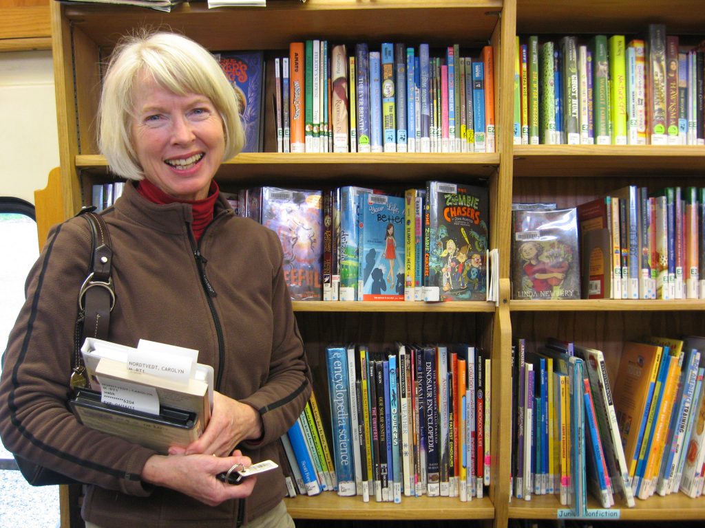 image of woman standing in front of bookshelf holding books