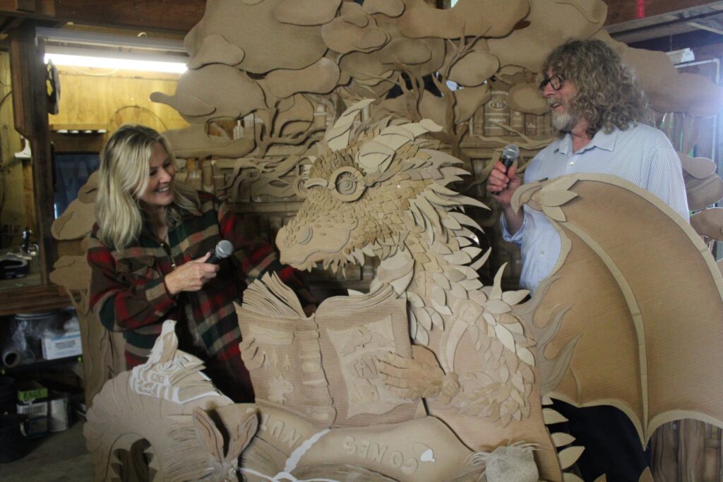 cardboard dragon sculpture with artist and interviewer