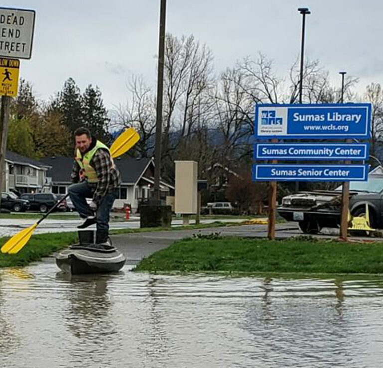 Man riding a kayak in flooded library parking lot